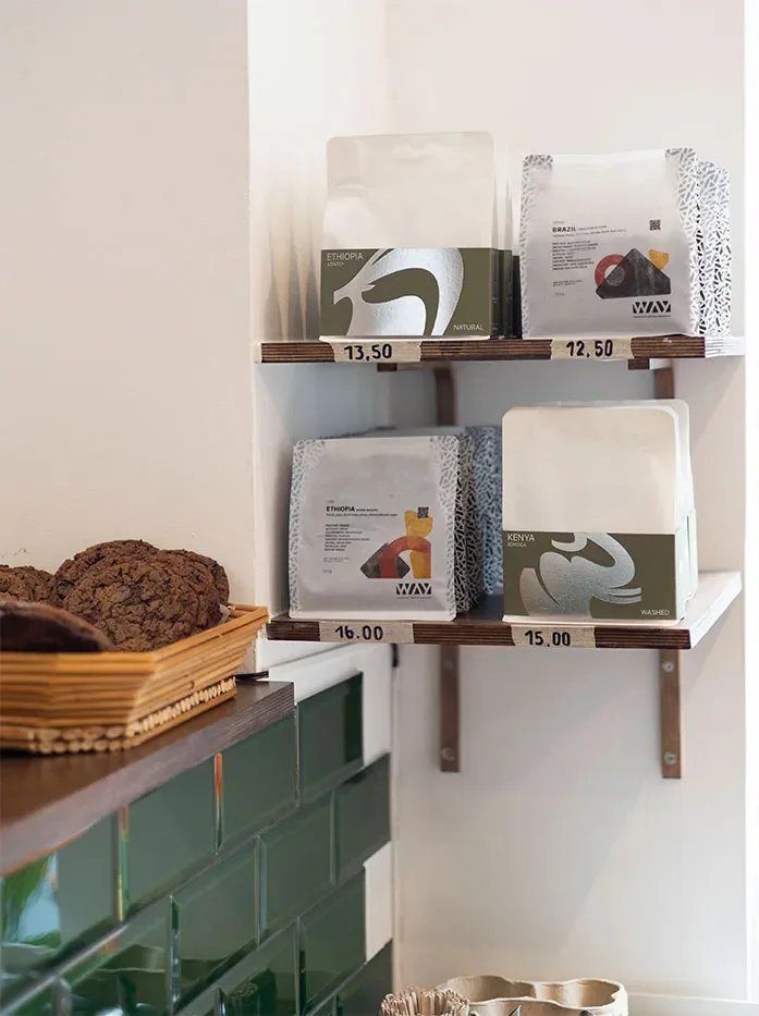Bags of coffee beans on two shelves, above the bar's green tiles