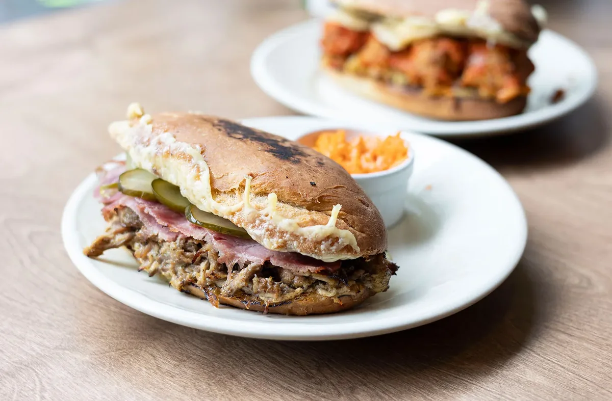 Pulled pork sandwich with ham, pickles and melted cheese on a white plate