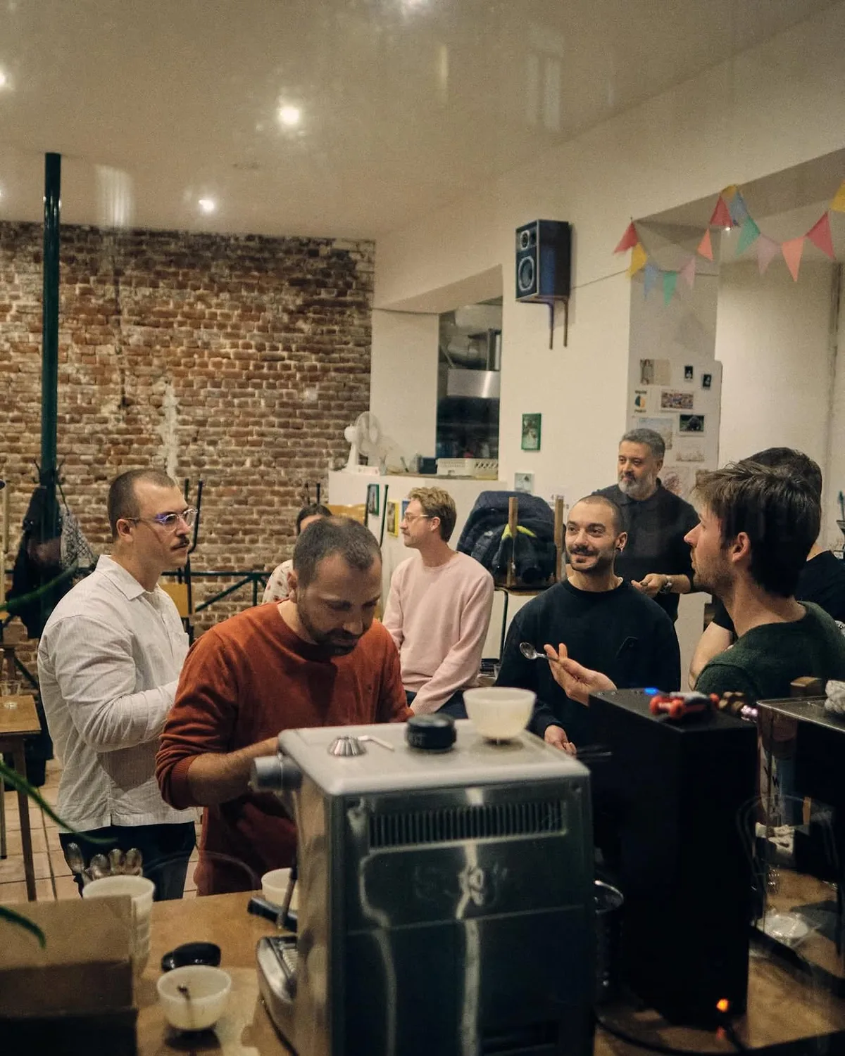 Une dizaine de personnes autour de la table de cupping, devant le mur de brique