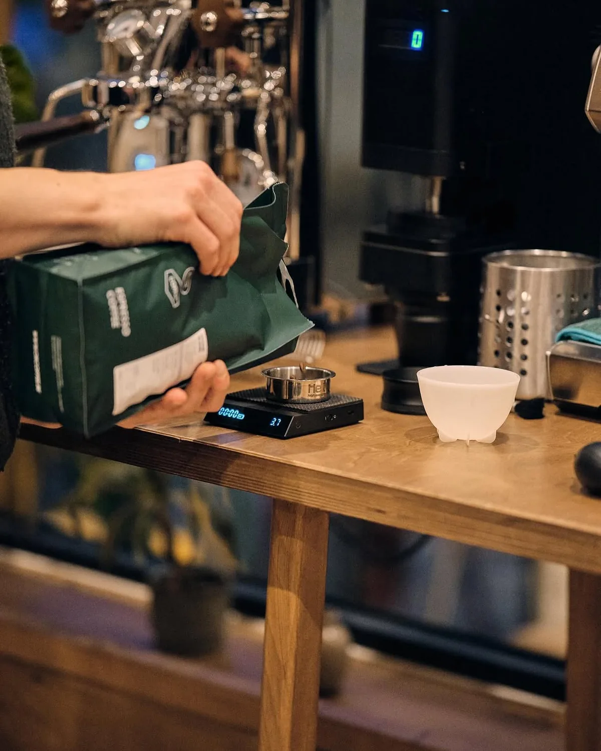 Des grains de café versés d'un sachet vert sur une balance de précision